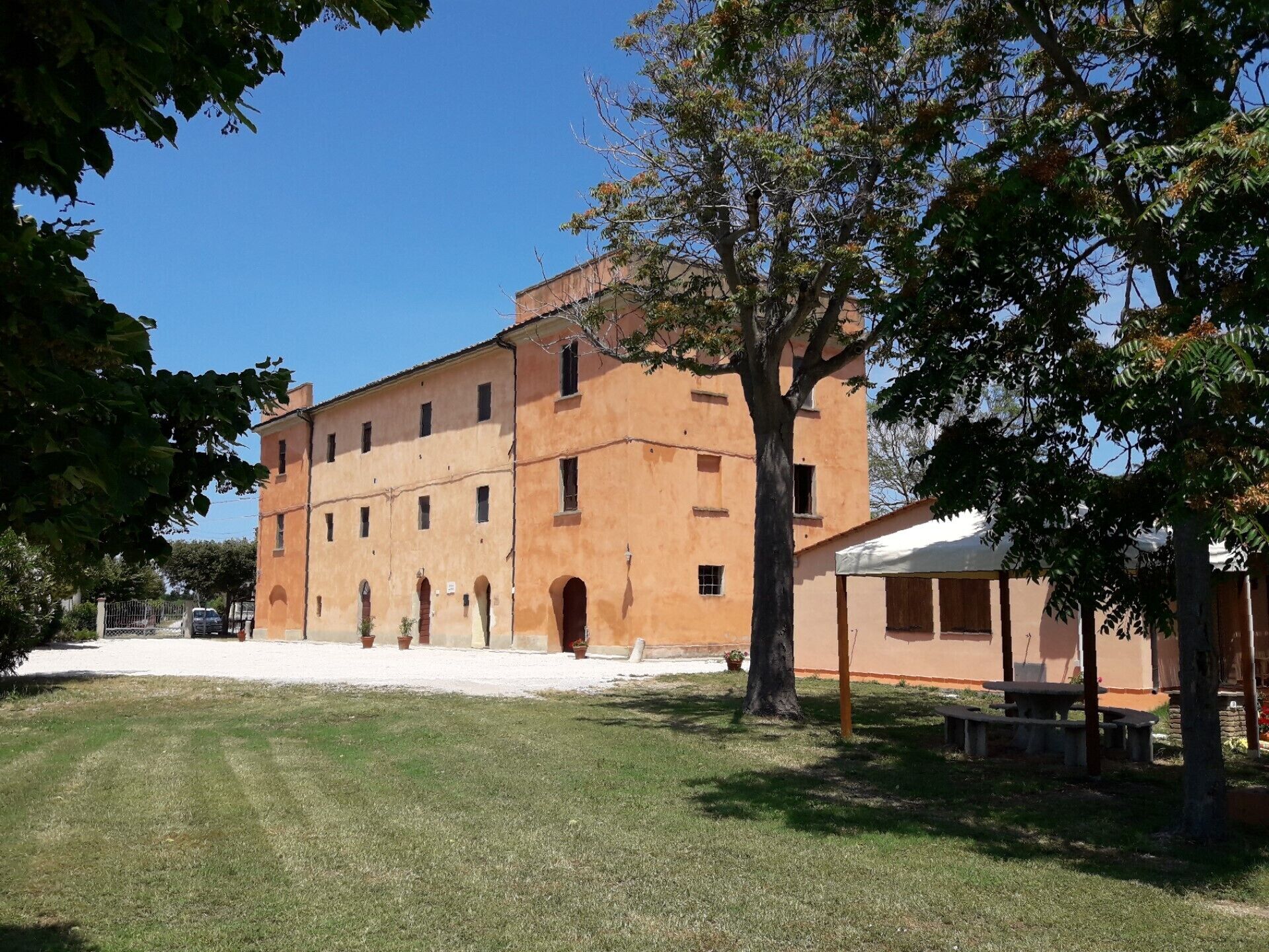 A large, multi-story building with a flat roof and arched windows, surrounded by a grassy area and trees.