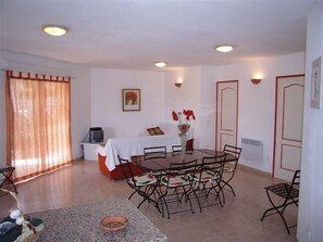 A dining area with a table and chairs, a bed with a red headboard, and a television on a stand.