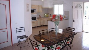 A compact kitchen with a dining area, featuring a glass-top table and chairs, a microwave, and a small island with a vase of flowers. - Villa Cigale 3 - 8 people 300m from the beach with shared pool (San-Nicolao)