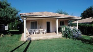 A single-story house with a tiled roof, a covered patio with a table and chairs, and a small garden area. - Villa Cigale 3 - 8 people 300m from the beach with shared pool (San-Nicolao)