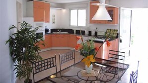 A modern kitchen with orange cabinets, a glass dining table, and a vase with flowers. - Villa Cigale 3 - 8 people 300m from the beach with shared pool (San-Nicolao)