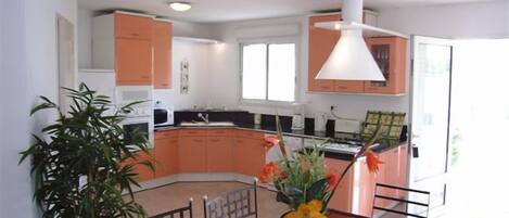 Una cocina moderna con gabinetes naranjas, una mesa de comedor de vidrio y un jarrón con flores.