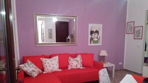 A room with a red sofa, a white table, a mirror, and a lamp. - CASE COLOMBO AND MATTARELLA central apartment with wi-fi and free parking space (San Vito Lo Capo)