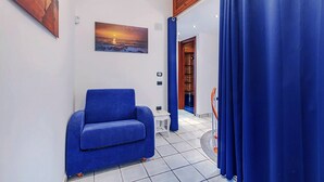 Un pasillo con un sofá azul, un cuadro de una puesta de sol y una puerta de madera.
