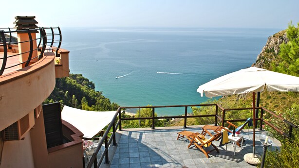 Una terraza con vista al mar, mobiliario exterior y un paraguas blanco.