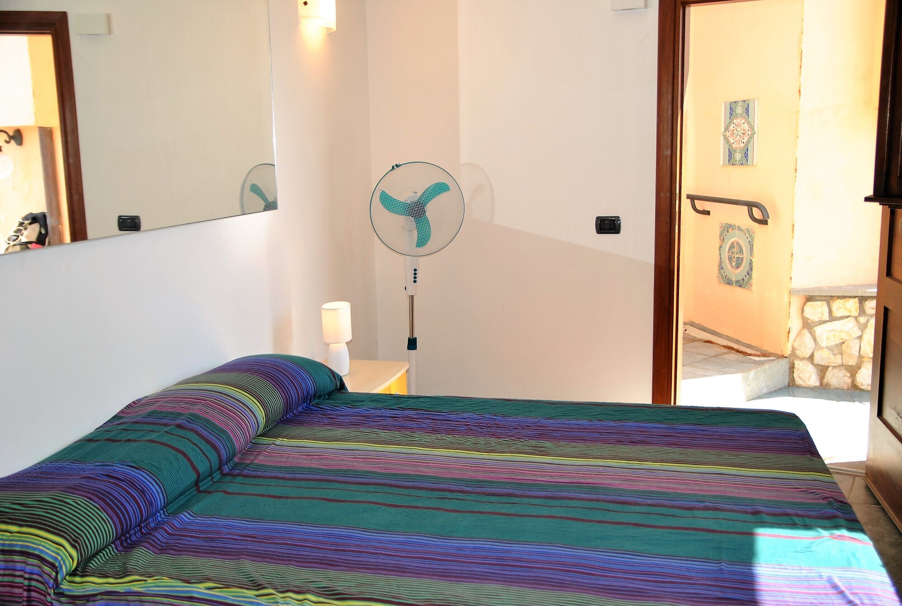 Una habitación con cama, ventilador, espejo y puerta que da a un balcón.