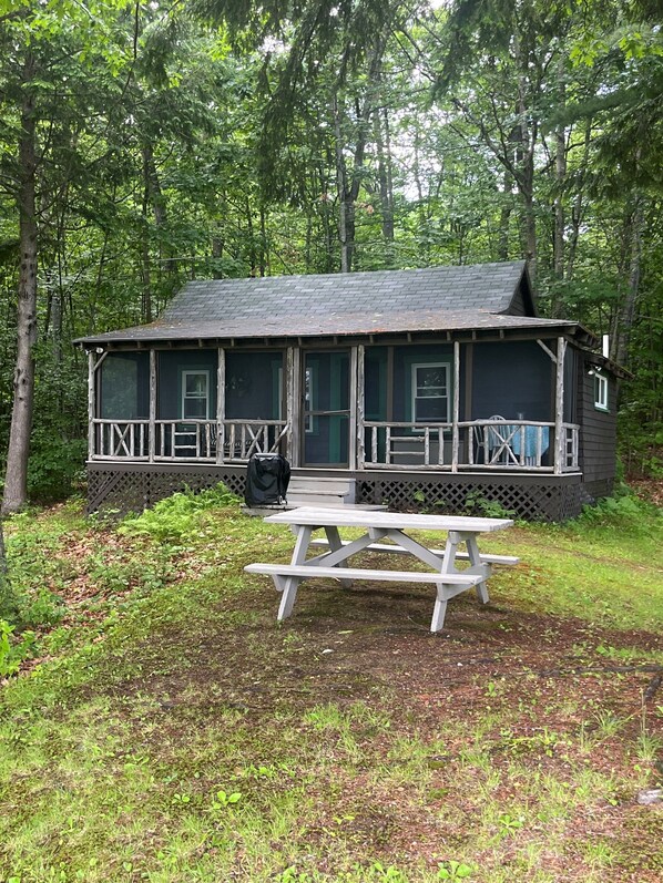 Ein rustikales Blockhaus mit Veranda, Picknicktisch und kleiner Terrassenfläche.