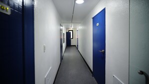 Un pasillo estrecho con puertas azules a ambos lados, suelo alfombrado y una luz en el techo.