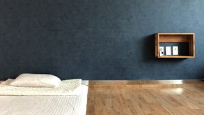 Una habitación con cama, suelo de madera, una pared oscura y un pequeño estante con objetos.