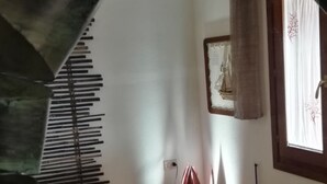 Ein Zimmer mit einer großen, spiralförmigen Treppe, die zu einer oberen Etage führt. Es gibt ein Bett mit einer gelb-rot karierten Tagesdecke, einen Nachttisch mit einer Lampe und ein Fenster mit einem Vorhang.