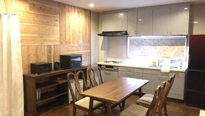 A compact kitchen with wooden cabinetry, a dining table with chairs, a microwave, and a window above the sink. - House Kira (Chatan)