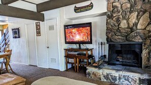 A living room with a stone fireplace, a television, and a wooden table.
