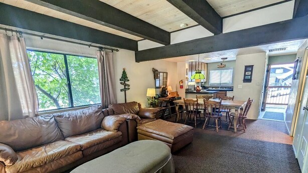 A living room with a brown leather sofa, a green ottoman, and a dining area with a table and chairs.