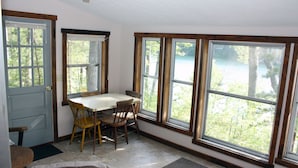 Un coin repas avec une table et des chaises, de grandes fenêtres à cadres en bois et une vue sur les arbres à l’extérieur.