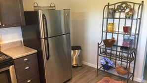 Eine kompakte Küche mit Edelstahlkühlschrank, integriertem Backofen und einem Metallregal mit diversen Küchenutensilien.