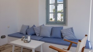 A room with a white stone floor, a blue sofa with striped cushions, a white table, and wooden chairs. - Chora villa 1 with unique sea view (Hora)