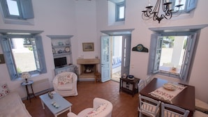 A cozy living room with a fireplace, white furniture, and a dining area with a table and chairs. - Chora villa 1 with unique sea view (Hora)