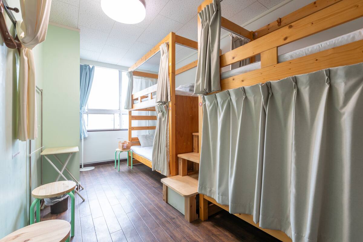 A dormitory room with bunk beds, a small table, and a chair.