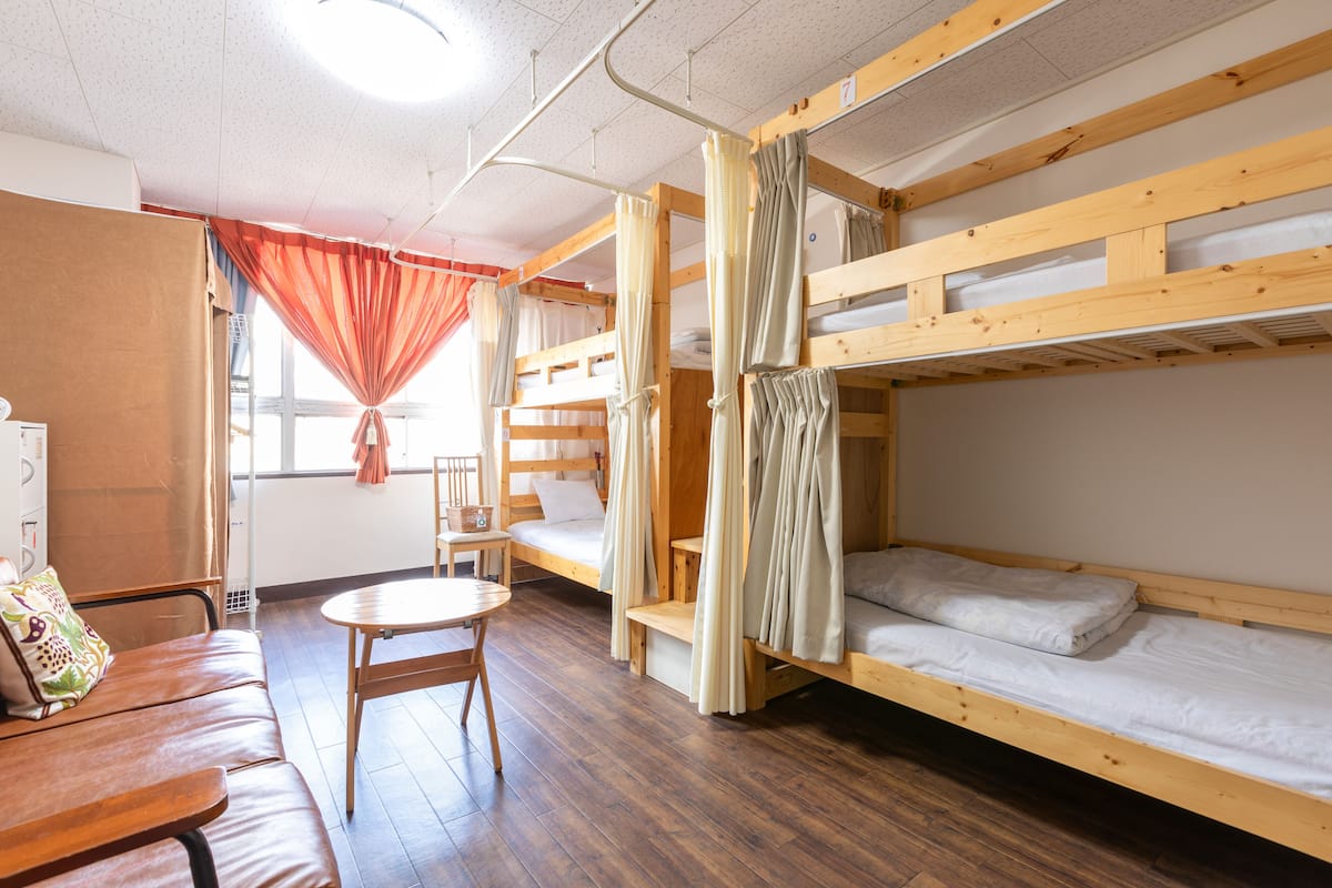 A dormitory room with bunk beds, a wooden table, and a sofa.