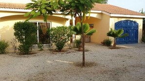 Una casa con camino de grava, un portón azul y varias plantas.