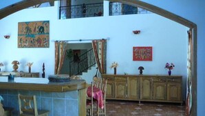 Un amplio salón con techo alto, una zona de cocina con barra, y un comedor con armarios de madera y suelo de baldosas.