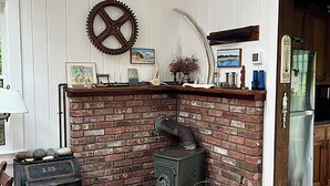A rustic kitchen with a brick fireplace, wooden cabinets, and a vintage stove. - Bright and cozy menemsha cottage (Chilmark)
