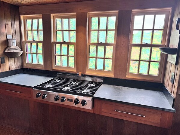 A kitchen with a gas stove, wooden cabinets, and large windows. - Bright and cozy menemsha cottage (Chilmark)