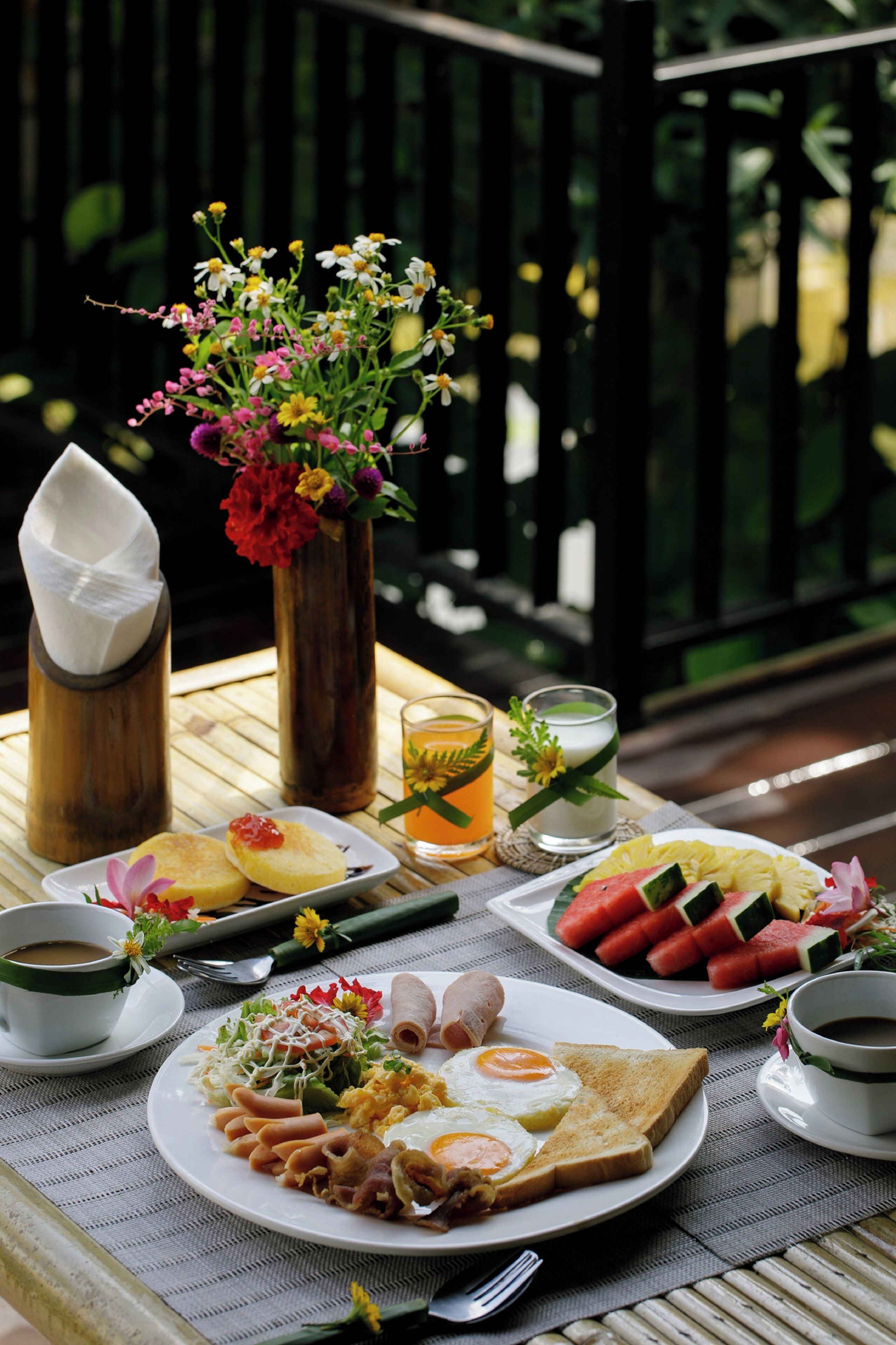 Una mesa dispuesta con diversos alimentos para el desayuno, como huevos, tostadas y fruta, acompañada de bebidas y un centro de mesa floral.