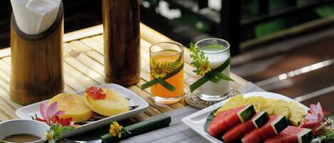 Una mesa dispuesta con diversos alimentos para el desayuno, como huevos, tostadas y fruta, acompañada de bebidas y un centro de mesa floral.