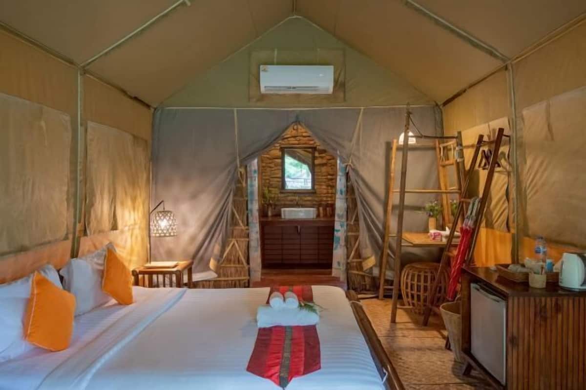 A tented accommodation with a bed, a small table, a shelf with items, and a window.