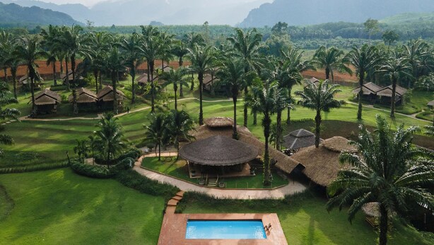 Un resort con cabañas de techo de paja, una piscina y abundante vegetación.