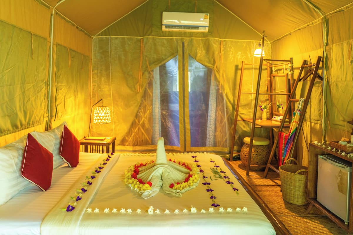 A tented room with a bed, pillows, a table with a lamp, a ladder, and a basket.