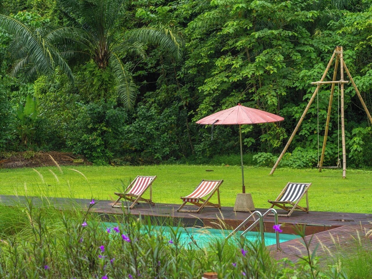 A pool area with three striped lounge chairs and a red umbrella.