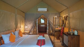 Habitación tipo alojamiento con tienda de campaña, cama, mesita pequeña, lavabo y espejo.