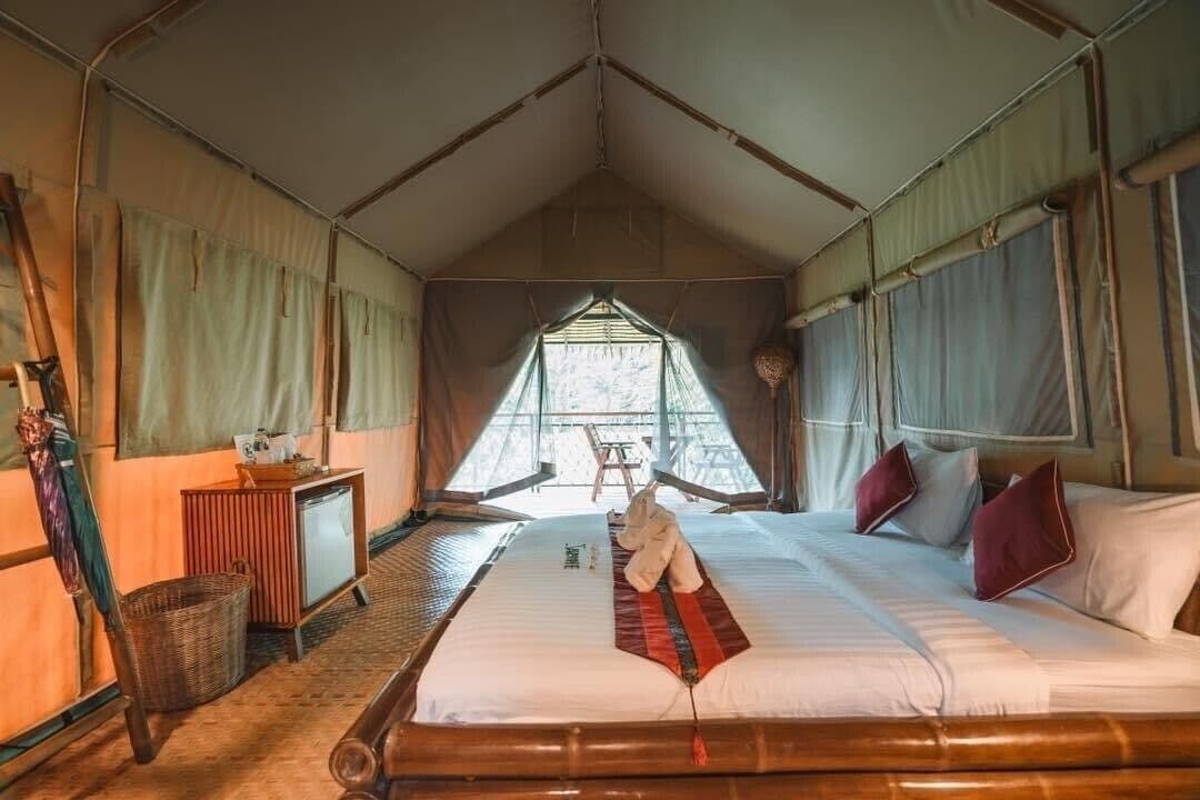 A tented accommodation room with a bed, a small desk, and a window.