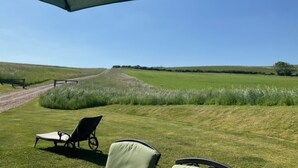 A grassy outdoor area with a path leading to a distant view, two lounge chairs, and a large umbrella.