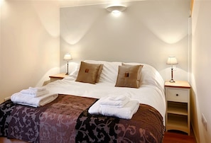 A neatly made bed with two pillows, a bedside table with a lamp, and a small drawer unit.