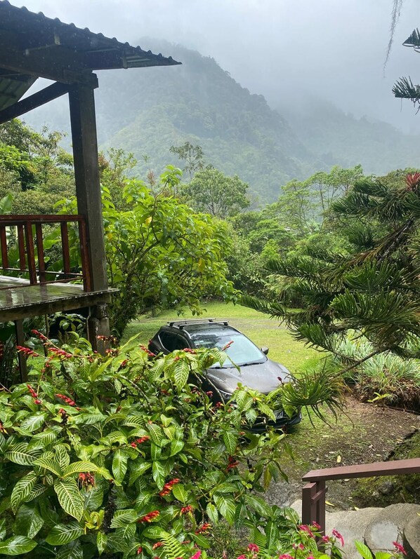 A car parked in a lush, green garden with a wooden pergola and a view of misty mountains. - One Bedroom Cabin On Two Hundred Acres in costa rica (CACHI)