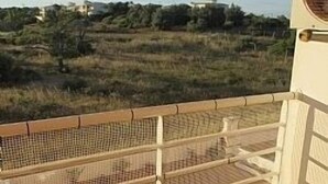 A balcony with a wooden chair, a mesh safety barrier, and a view of a natural landscape with trees and buildings in the distance. - 1 Bedroom Apartment Can Sleep 4 People With Private Pool And Air Conditioning (Armação de Pêra)