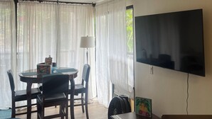 Un soggiorno con zona pranzo, una TV a schermo piatto montata al muro, una ventola e un tavolo con sedie.