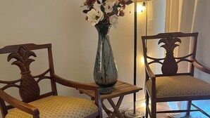 Due sedie in legno con motivi di ananas, un vaso di vetro con fiori e una lampada da terra in una stanza con pavimento in legno.