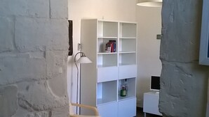 A room with a white bed, a desk, a chair, a lamp, and a white shelving unit with books and a bottle. - Palazzolo Acreide Charming cottage for two people !!  (Palazzolo Acreide)
