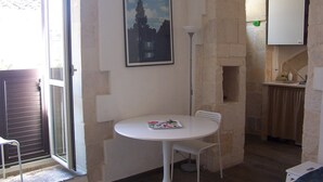 A small room with a round white table, a white chair, a framed picture on the wall, and a small kitchen area with a cabinet and a sink. - Palazzolo Acreide Charming cottage for two people !!  (Palazzolo Acreide)
