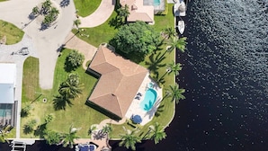 Luftaufnahme eines Anwesens an der Küste mit Swimmingpool, Palmen und Bootssteg.