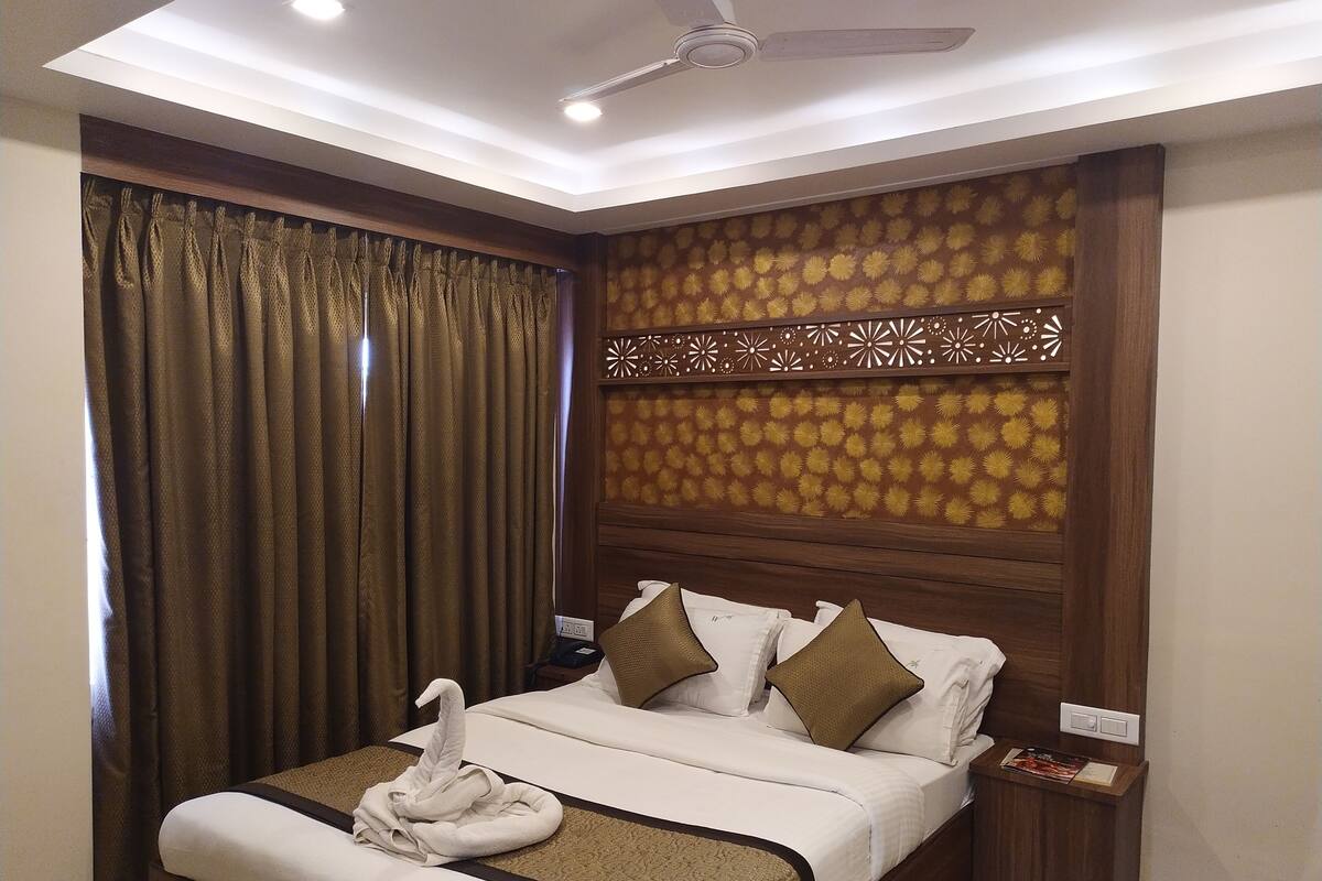 A hotel room with a bed, curtains, a ceiling fan, and a decorative wall panel.