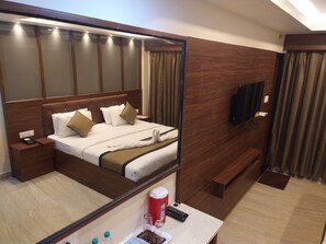 A hotel room with a large bed, a bedside table with a phone and remote controls, a mirror, a TV mounted on the wall, and a small table with a bottle and remote. - Hotel White Boutique (Puducherry)