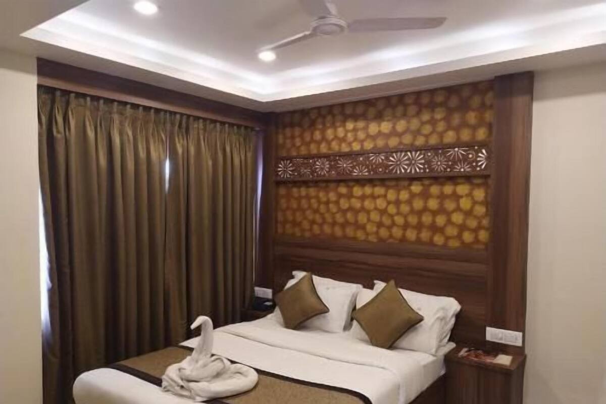 A hotel room with a bed, curtains, a ceiling fan, and a decorative wall panel.