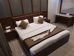 A neatly made bed with white and brown bedding, a headboard with a phone, and a bedside table with a lamp.