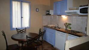 A compact kitchen with a dining table and chairs, a microwave, and a clock on the wall.