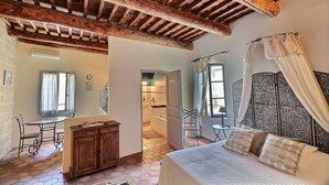 A bedroom with a wooden ceiling, a bed with patterned pillows, a bedside table, and a window with curtains.
